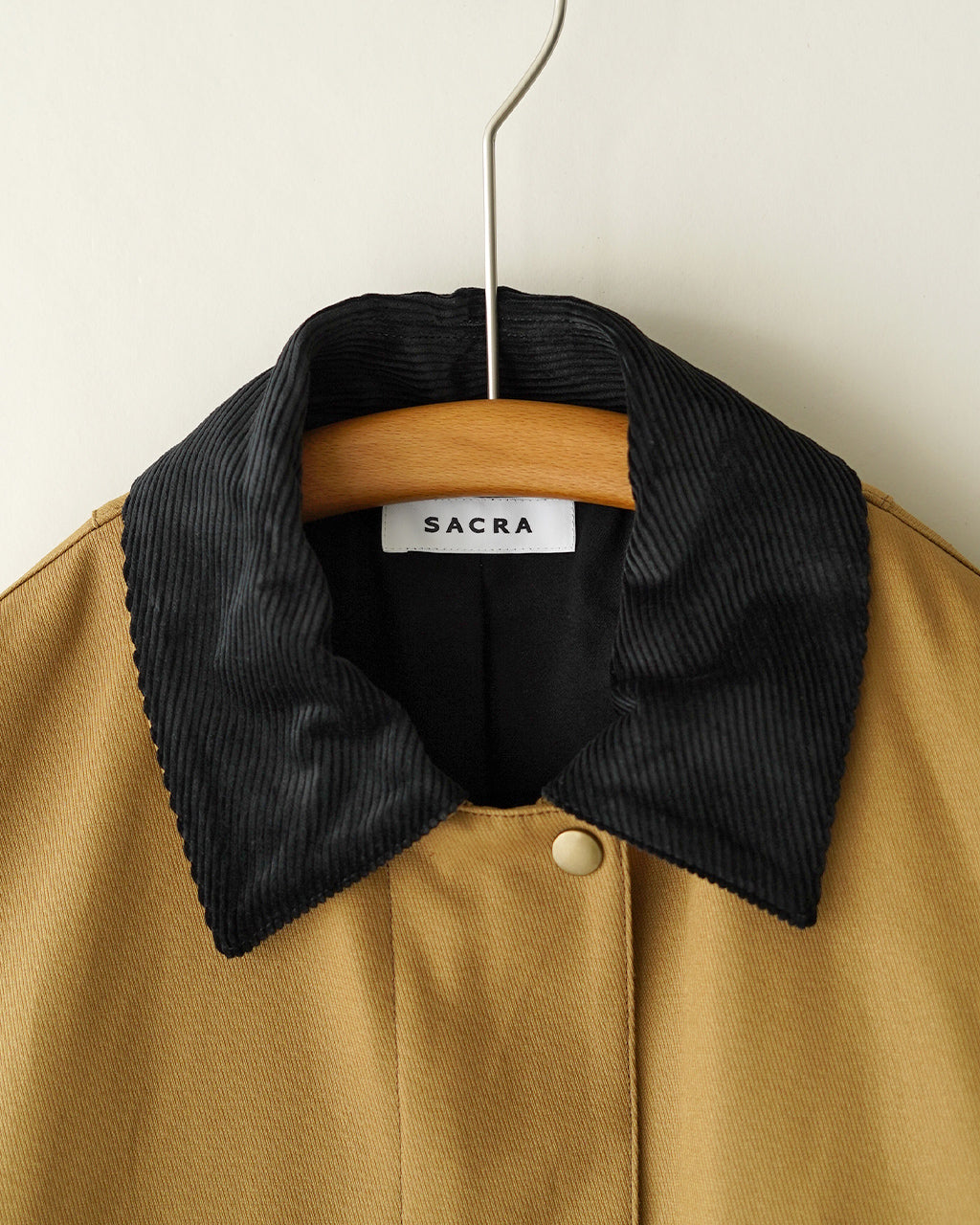 ベージュのコットンツイル生地に、黒のコーデュロイ風襟が際立つカバリーツイルジャケット。 hanger に掛かったデザインで、襟元のディテールが強調されている正面ショット。