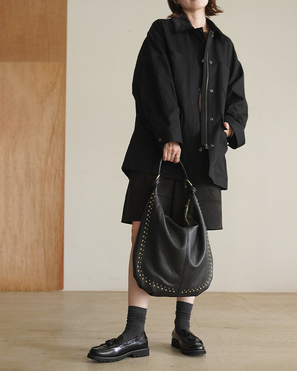 ブラックのCAVALRY TWILL JACKETを着こなす女性の横からの姿。ゆったりとしたオーバーシルエットと襟付きデザインが特徴で、裾まで見える着丈感と袖のボリュームが分かる。