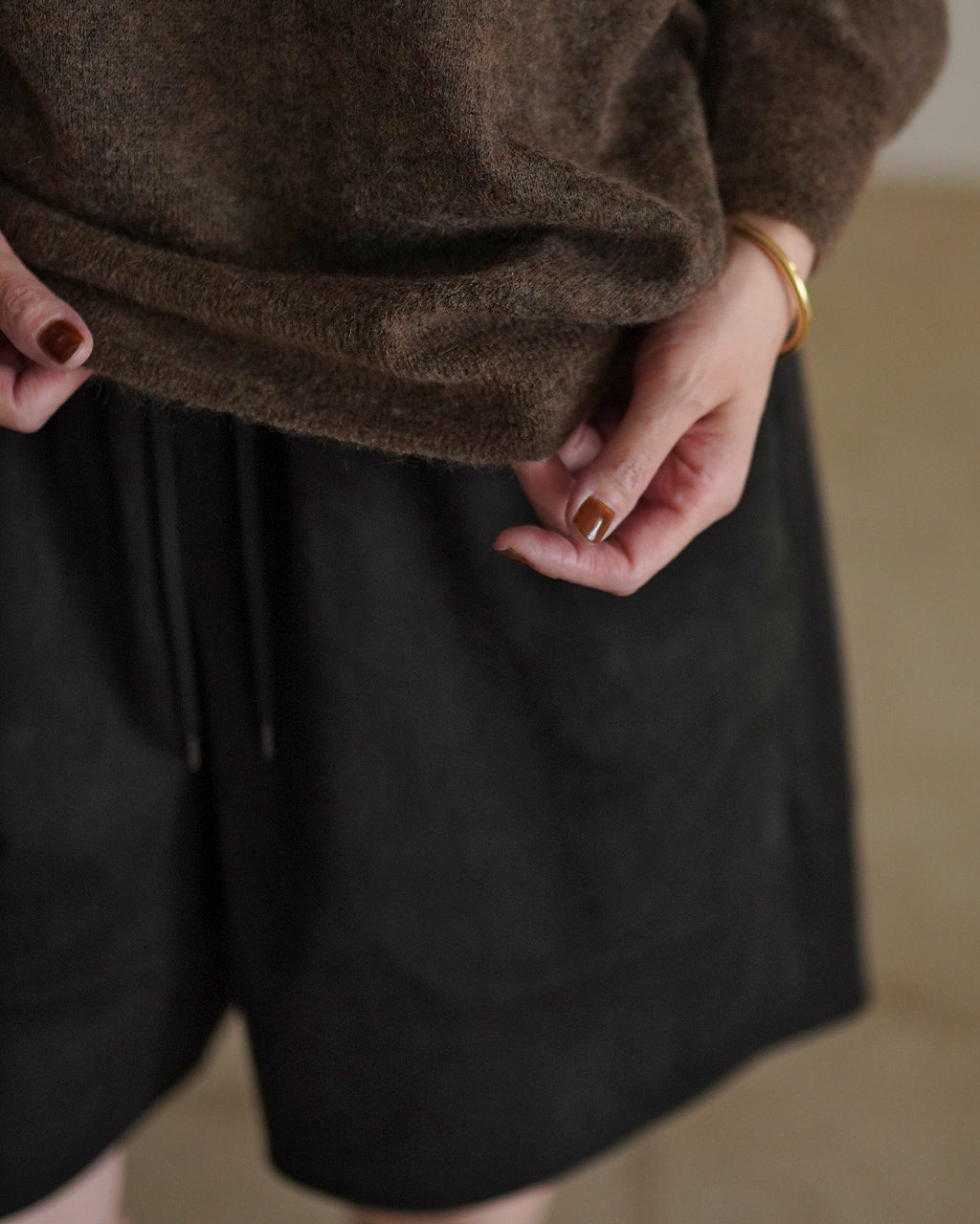 ブラウン系モヘアトップの腰まわりを映すアップ。ふわりとした毛足の質感とボーダーの細やかなディテールが見えるシーン。手元にはゴールドのブレスレットがあり、裾がやや持ち上がっている。