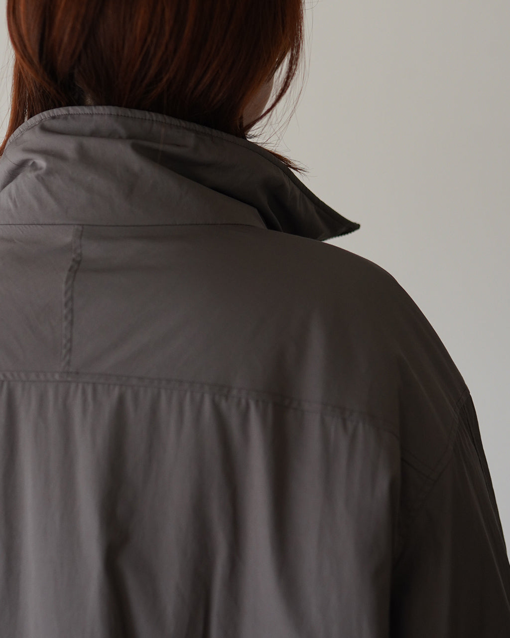 SACRA padding-taffetaコートの後ろ姿。カーキ系のタフタ生地で、肩から背中にかけての切り返しと程よいボリューム感が分かる。