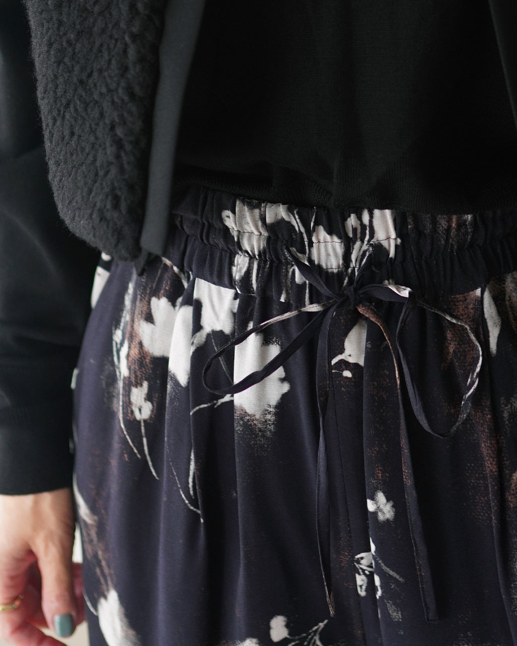 黒地に花柄のワイドパンツ。ウエストはゴム入りで絞り紐が見え、ドレープ感のある素材がシルエットを演出するディテール画像