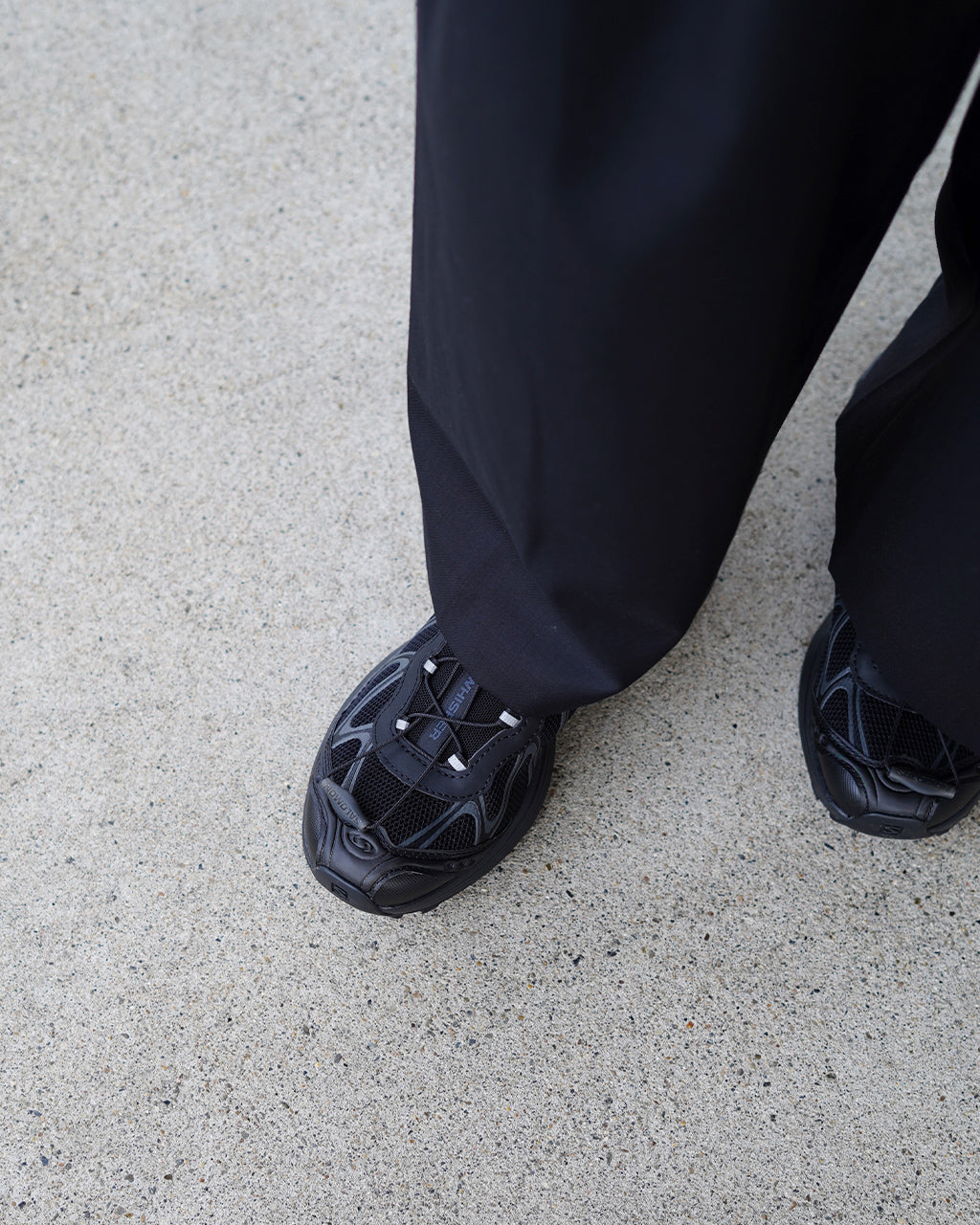黒系のスニーカーとパンツの足元アップ。立体的な靴底のディテールと素材感が分かる着用風景。