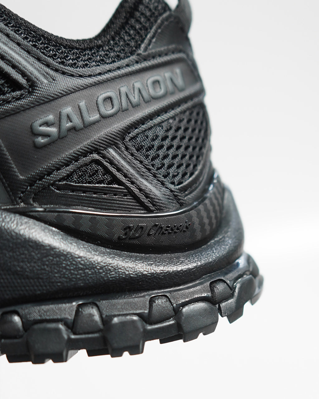 SALOMONのブラック系スニーカーのアップ。革新的なメッシュ素材と厚めのソールが特徴で、ヒール部分にブランドロゴが立体的に配置されています。