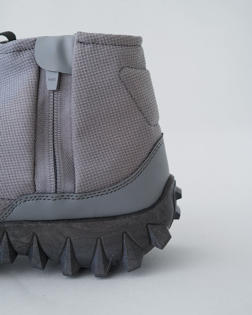 サロモン SNOWCLOG MID の側面アップ。グレー系のテキスタイルアッパーと太めのソールに特徴的な断面が映える、履き口近くのジッパーとYKKタグのディテールが見える。