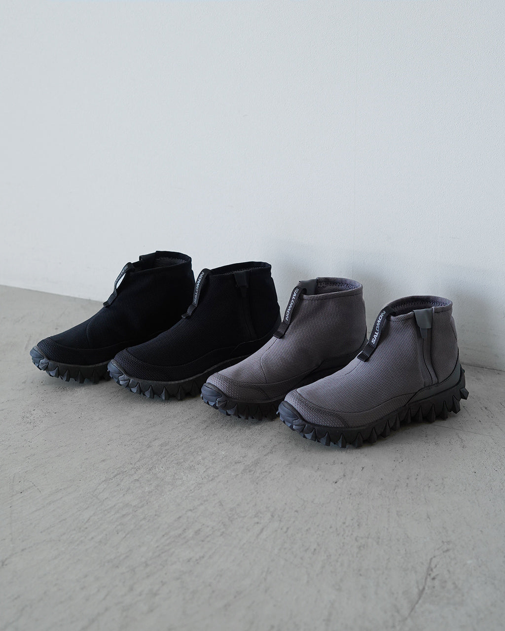 サロモン SNOWCLOG MID のブラック系とグレー系のショートブーツが並ぶ、伸縮性のあるアッパーと分厚いソールのディテールが特徴的な着用感のイメージ