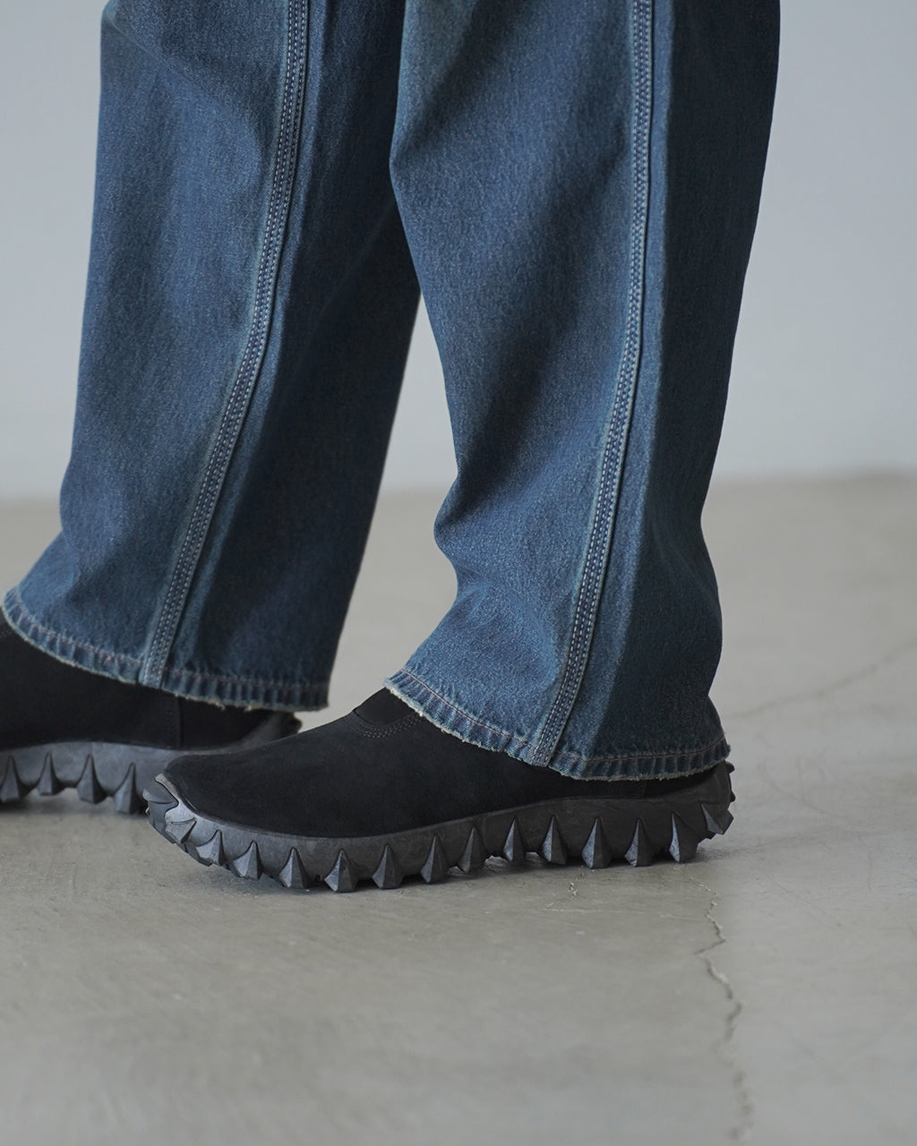 黒いスニーカーの横からのアップ。デニムパンツの裾を覆う程の丈感で、凹凸のあるソールが目を引くデザインです。