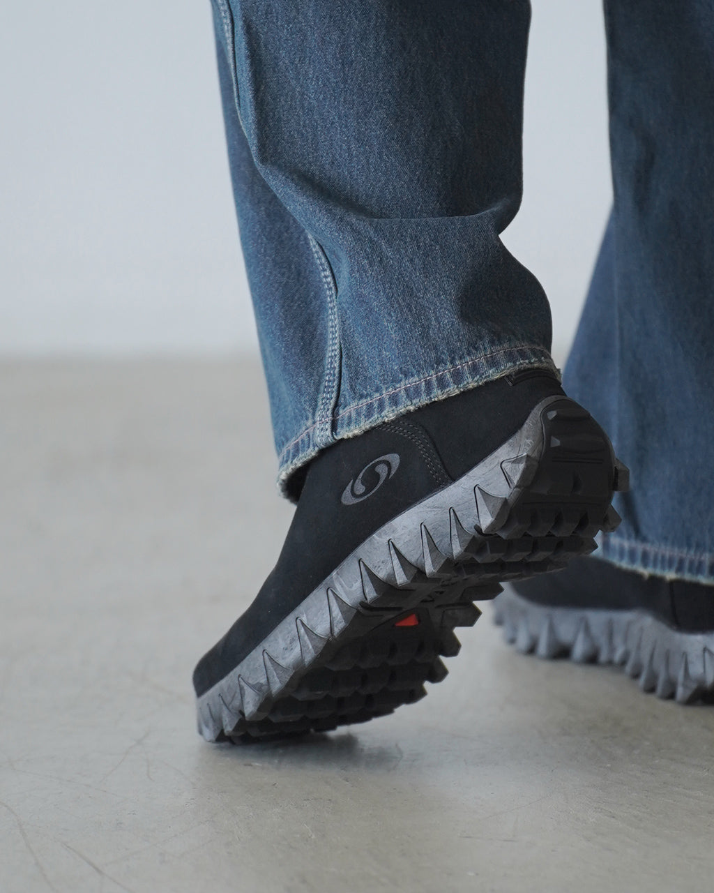 サロモン SNOWCLOG OG の内側へ覆うデニムパンツとスニーカーの接写。黒系のアッパーと凹凸のあるソールが視認できるディテール画像