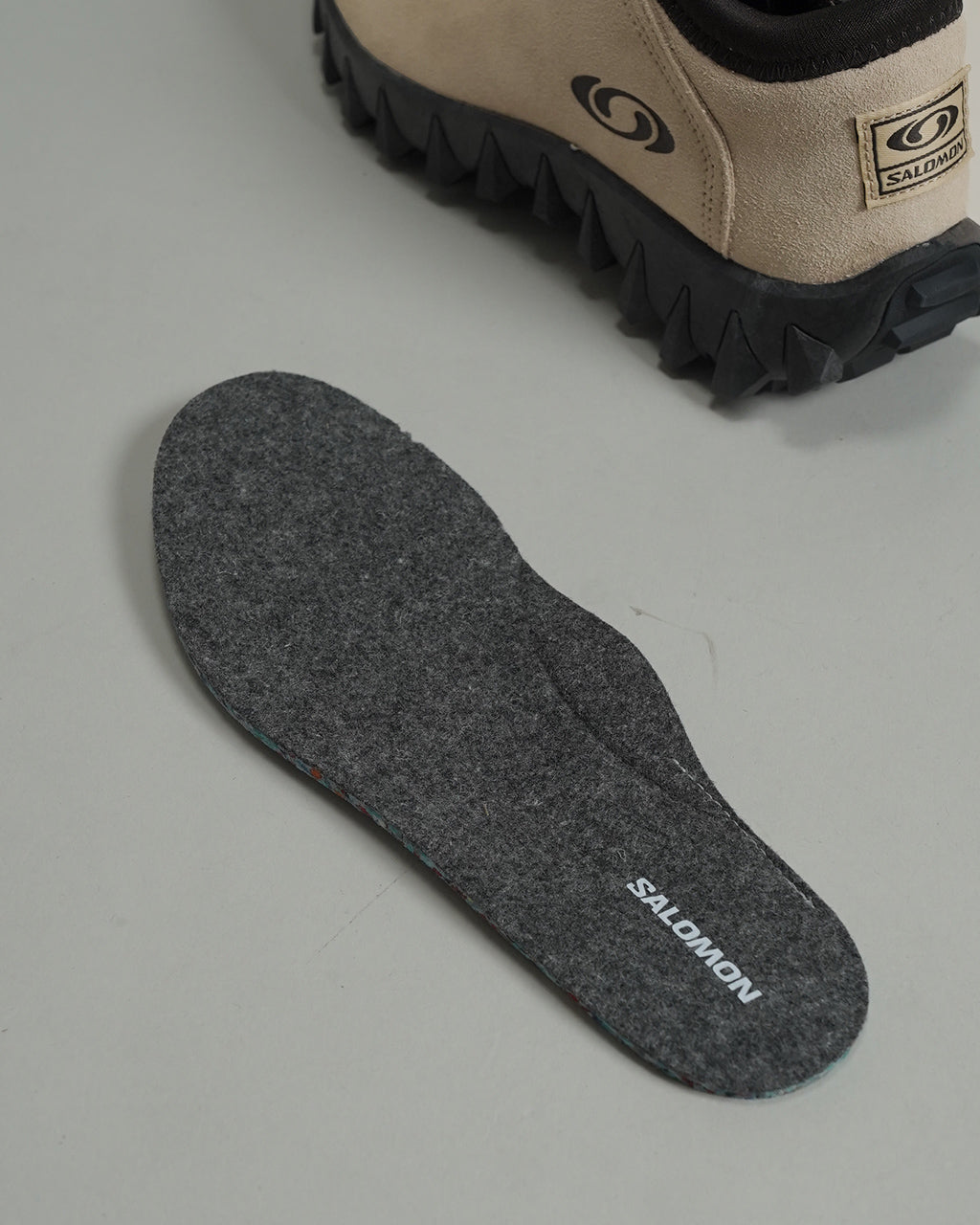 サロモン SNOWCLOG OG のベージュ系アッパーと黒いソールを横から見た写真。アウトソールの特徴的なデザインが視認でき、ブランドロゴが側面に入る様子も確認できる。