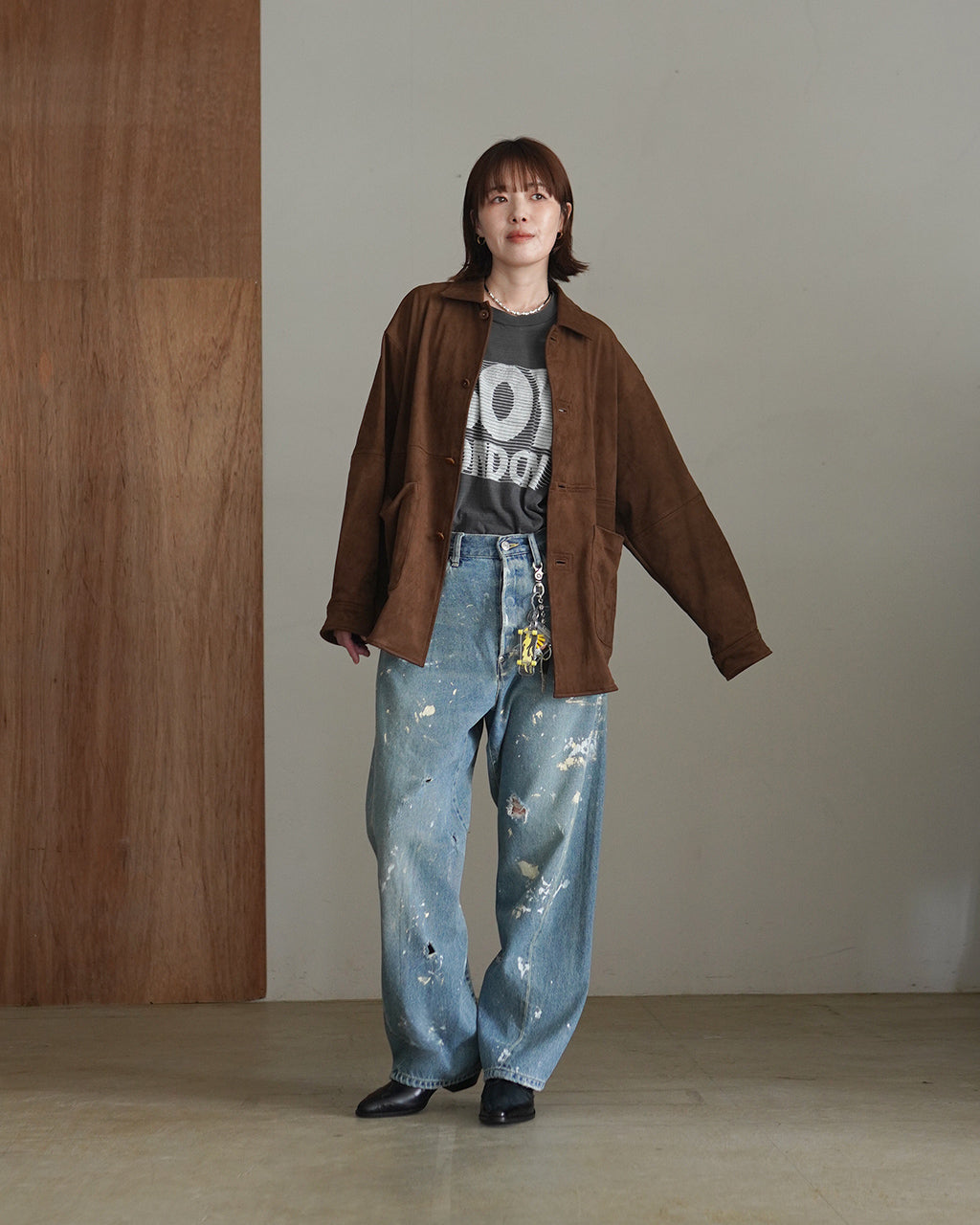 ライトブルーのバックシンチ付きデニムパンツを着用した女性モデルの全身写真。ゆったりとしたシルエットと裾まで落ちるラインが特徴的。 brown系のオーバーサイズジャケットとグレーのＴシャツを合わせたコーディネート。