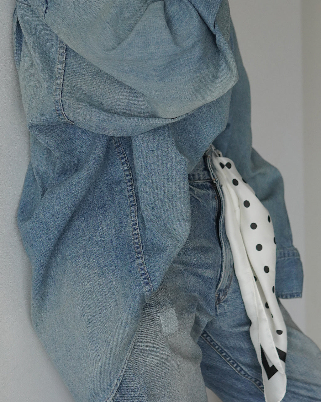 ライトブルーのOVER SIZE DENIM SHIRTの背面寄り。ゆとりのあるデニム生地と広めの襟元が特徴で、ウエスト寄りのポケット縁が見える。袖口や縫い目のディテールも確認できる写真。
