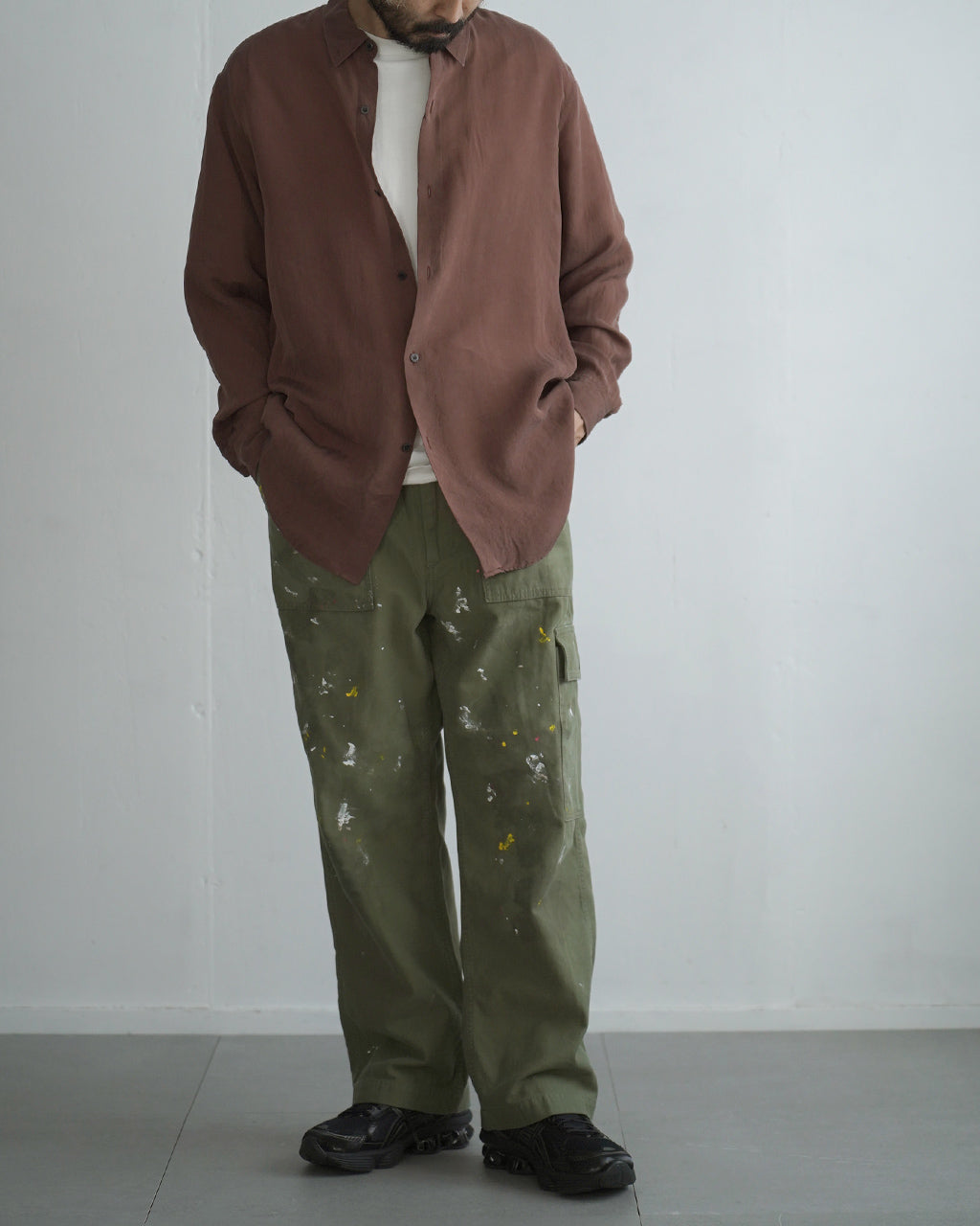 カーキ色のペイント風加工が特徴のパンツを着用した男性モデル。胸元に白Tシャツをのぞかせ、ゆったりとしたシルエットで脚元には黒いシューズ。