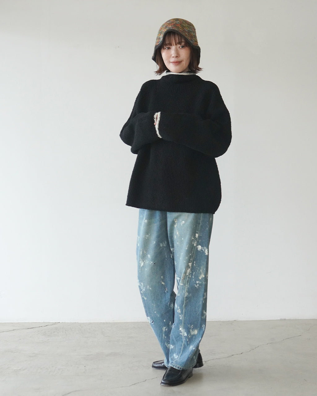 黒のニットに帽子を合わせたモデル。ゆったりとしたシルエットで袖口は白のリブが覗く。下にはブルーのダメージデニムを着用した着用イメージ。