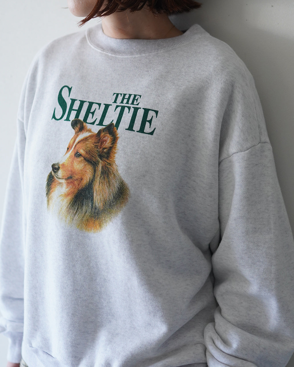 グレーのスウェットにTHE SHELTIEのロゴと犬の横顔プリントが入った、ゆったりシルエットのクルーネック袖周りはリブ仕様で着心地の良い一枚