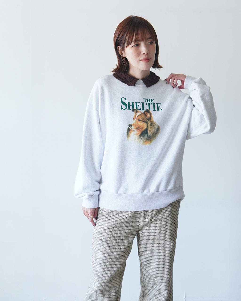 白色のスウェットに犬のモチーフとTHE SHELTIEのロゴがプリントされたデザイン。落ち着いた色味でリラックス感のある着用イメージ。